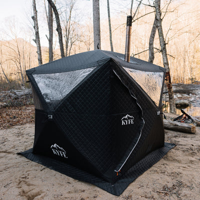 Black KYFE portable sauna tent set up on sand with forest background, wood-burning sauna tent